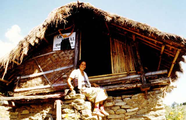 Alexandra in Nepal, auf den Stiegen zu einer Hütte aus Stroh sitzend, an deren Front das Logo der NGO Öko-Himal hängt.